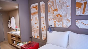 A hotel room with a bed, a red suitcase, a nightstand, and wall art depicting cityscapes.