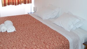 Habitación de hotel con cama, almohadas, una colcha y una ventana con cortinas.