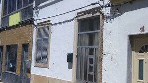 Un edificio de dos pisos con fachada blanca, una ventana visible con rejas de metal y una puerta con el número 16.