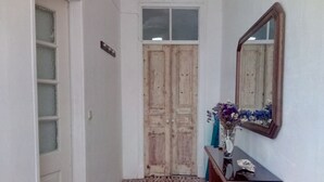 Un pasillo con baldosas de diseño, una puerta de madera, un espejo y un florero con flores sobre una consola de madera.