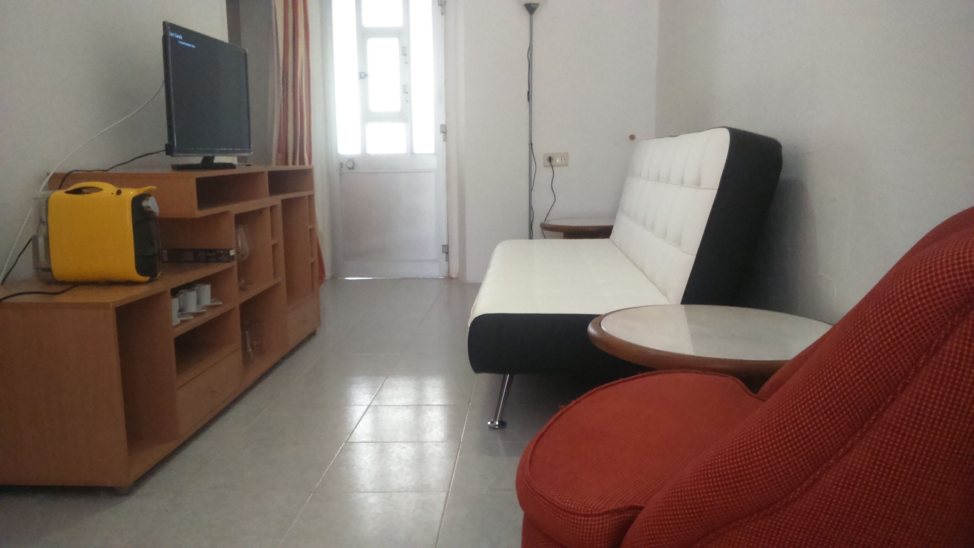 Un salón con un sofá, una mesita redonda, un televisor sobre un mueble de madera y una silla roja.