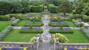 A formal garden with symmetrical pathways, manicured hedges, and a central fountain.