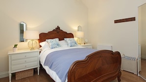 A bedroom with a wooden bed, two bedside tables with lamps, a nightstand, a mirror, and a radiator.