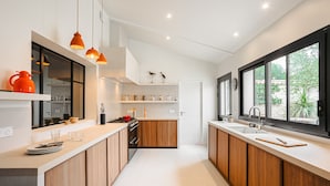 A modern kitchen with wooden cabinets, a central island, pendant lighting, and a view of greenery outside.
