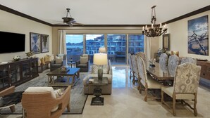 A spacious living room with a large television, comfortable seating, a dining area with a chandelier, and a view of a cityscape through large windows. - Dream Penthouse - Infinity Jacuzzi + Best View in Cabo (Cabo San Lucas)