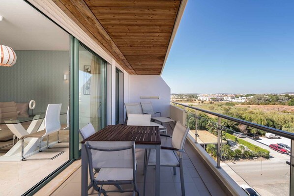 A balcony with a wooden ceiling, a glass table, and chairs.