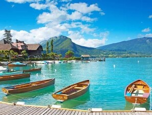 Een vakantieoord aan een meer met houten boten afgemeerd bij een steiger, omringd door bergen en helderblauw water.