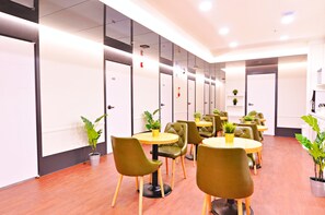 A modern hotel lobby with wooden flooring, green upholstered chairs, round tables, and potted plants. - OYO Hostel Myeongdong 3 (Seoul)