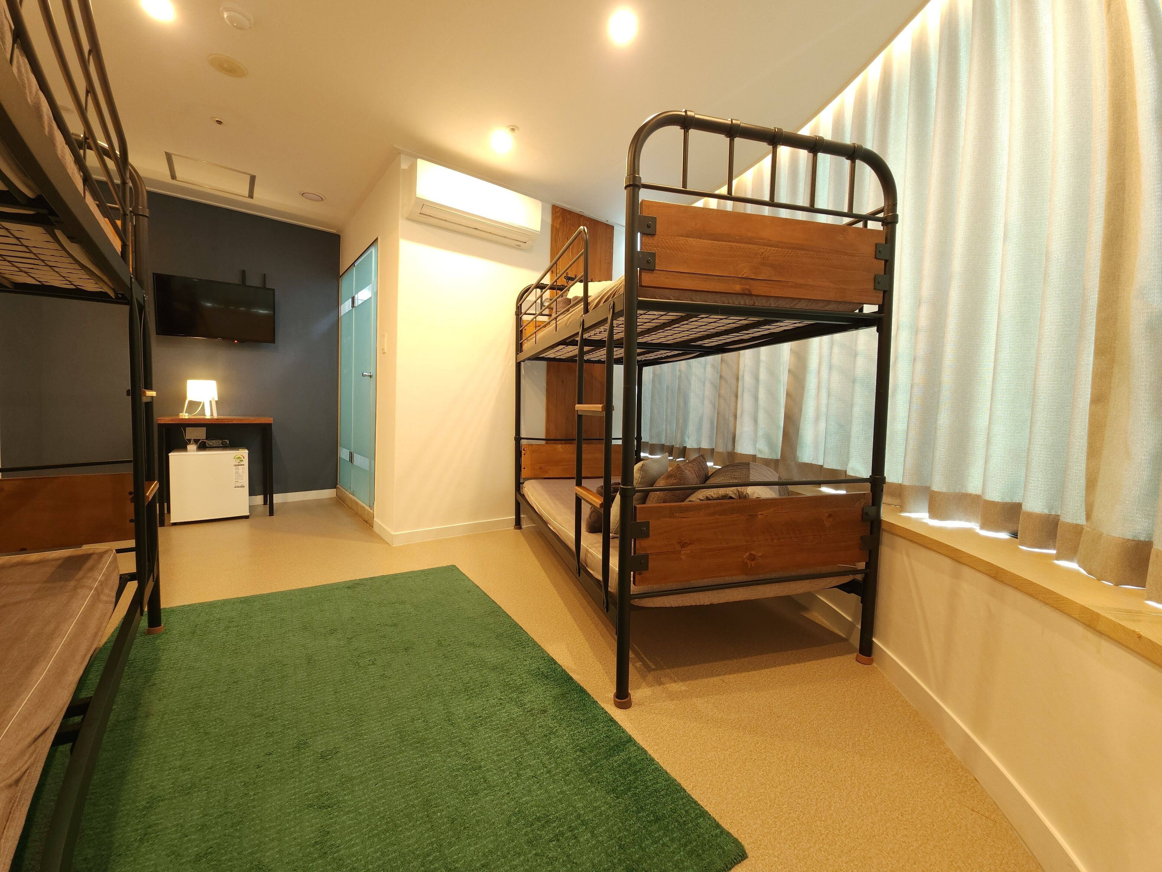 A bunk bed room with a desk, a small fridge, and a TV.