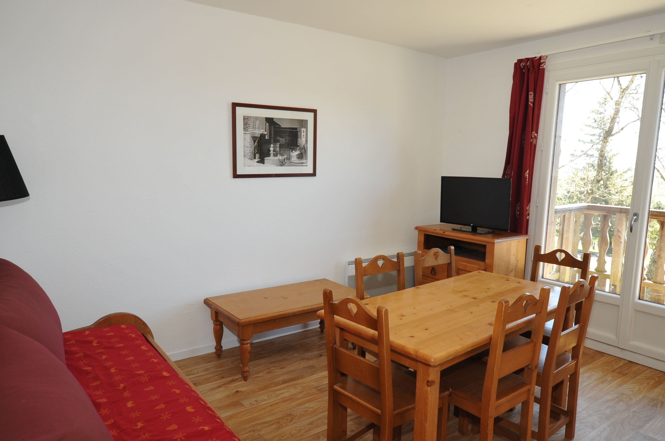 Een kamer met een houten eettafel, stoelen, een bankje, een televisie op een standaard, en een raam met gordijnen.