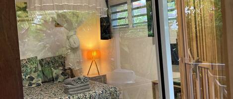 A bedroom with a bed, a bedside lamp, and a window with a view of greenery.
