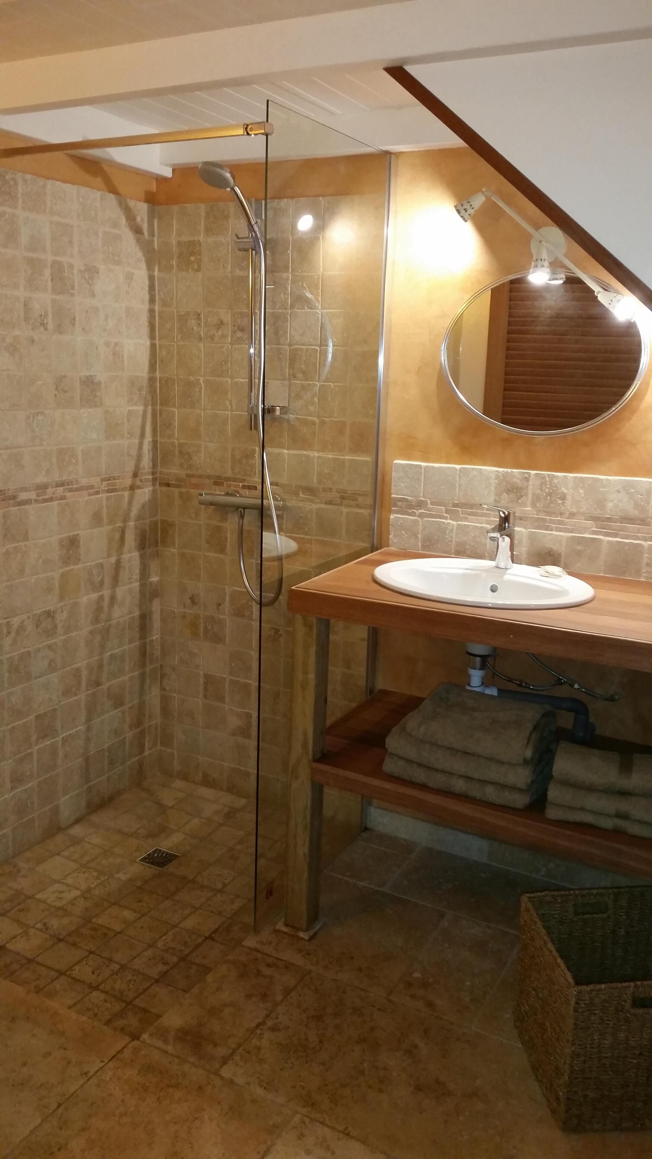 Un baño con ducha de vidrio, tocador de madera con lavamanos y espejo sobre el lavamanos.