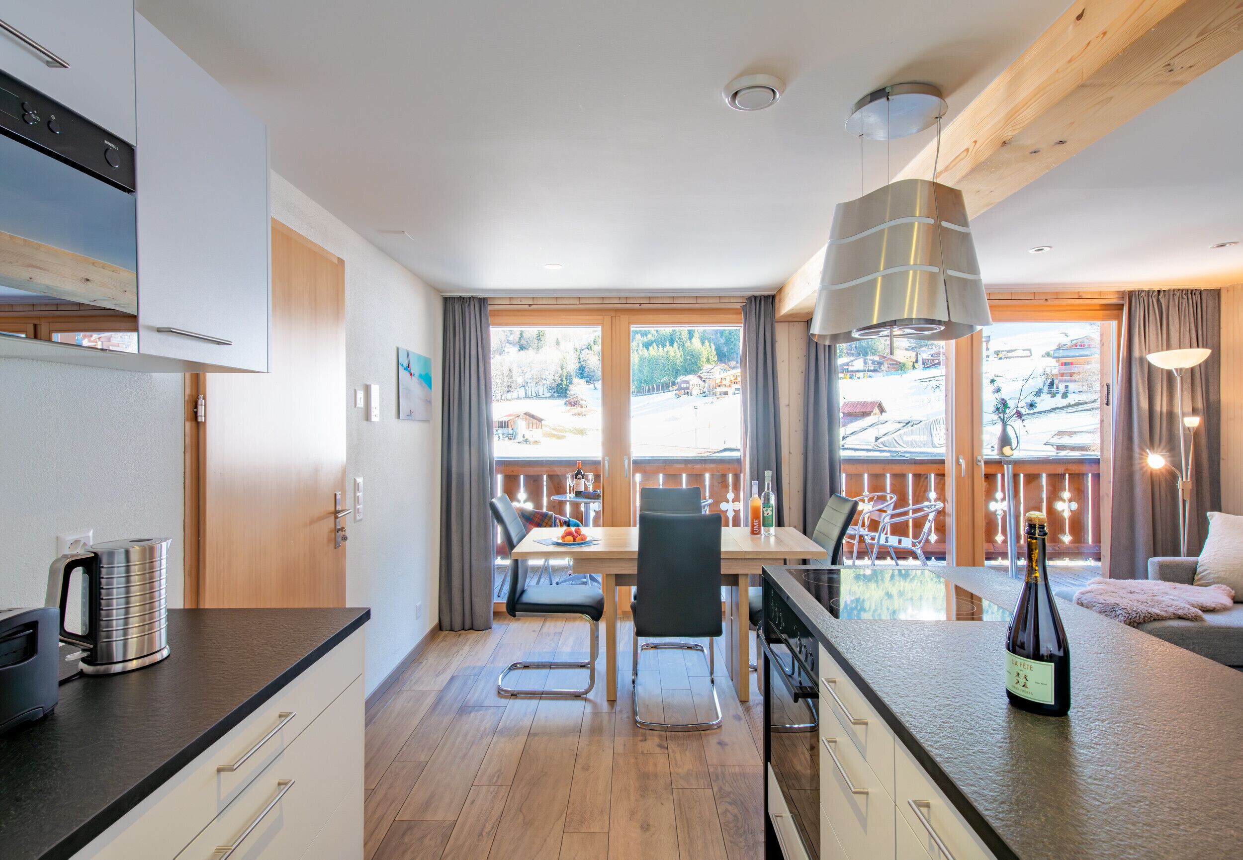 Une cuisine moderne avec un coin repas, un plancher en bois et de grandes fenêtres donnant sur un paysage enneigé.