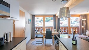 A modern kitchen with a dining area, wooden flooring, and large windows offering a view of a snowy landscape. - Chalet Belmont 7 - top location (Wengen)
