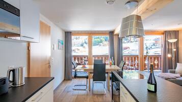 Une cuisine moderne avec un coin repas, un plancher en bois et de grandes fenêtres donnant sur un paysage enneigé.