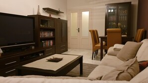 Ein Wohnzimmer mit Flachbildfernseher, Bücherregal, Esstisch mit Stühlen und einer Couch.