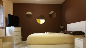 Ein Schlafzimmer mit einem Bett, einem Fernseher, einem Schminktisch und drei Wandspiegeln.