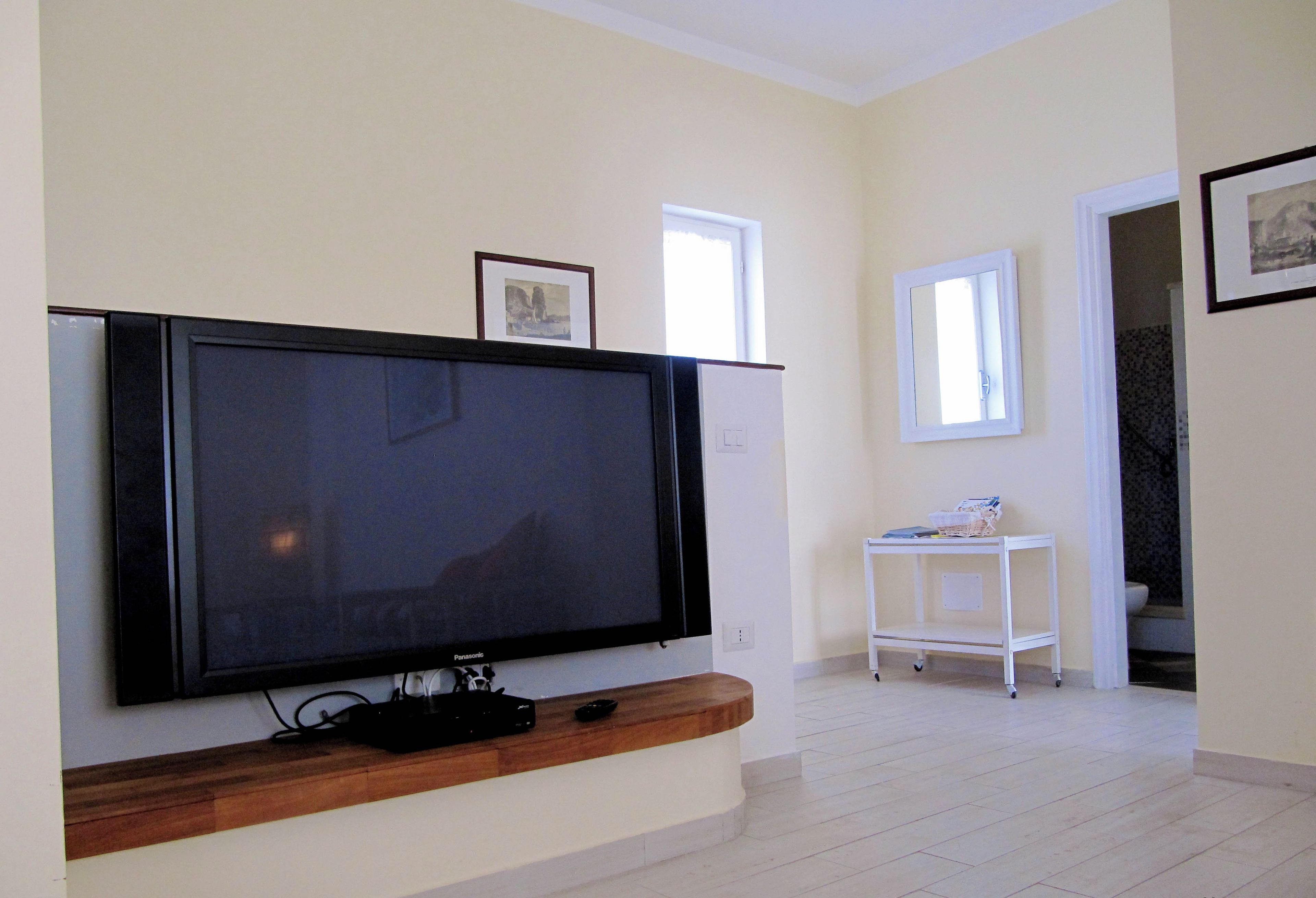 A living room with a large flat-screen TV mounted on the wall, a small white side table, and a framed picture above the TV.