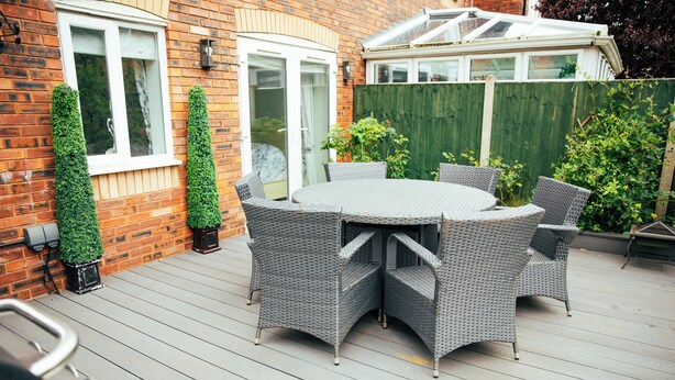 A patio with a round table and wicker chairs, surrounded by a wooden deck and a brick wall. - Delightful house in Stone, Staffordshire  close to lovely canal side walks.   (Stone)