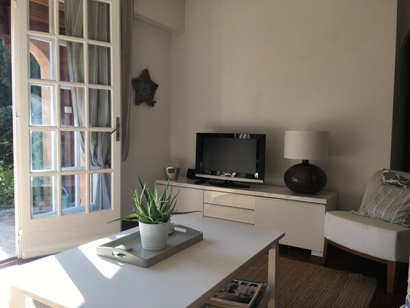 Un salon avec une télévision, une lampe, un canapé et une fenêtre avec des rideaux.