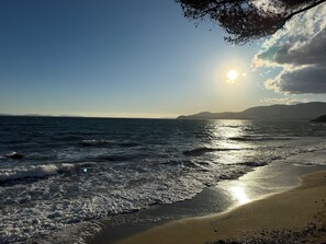 A beach with waves, a clear sky, and mountains in the distance.