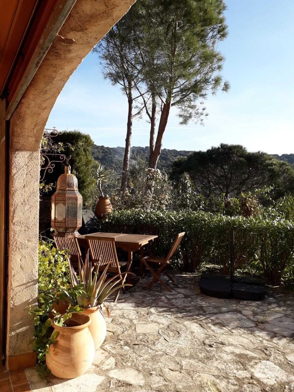 An outdoor patio with a stone floor, wooden furniture, and potted plants.