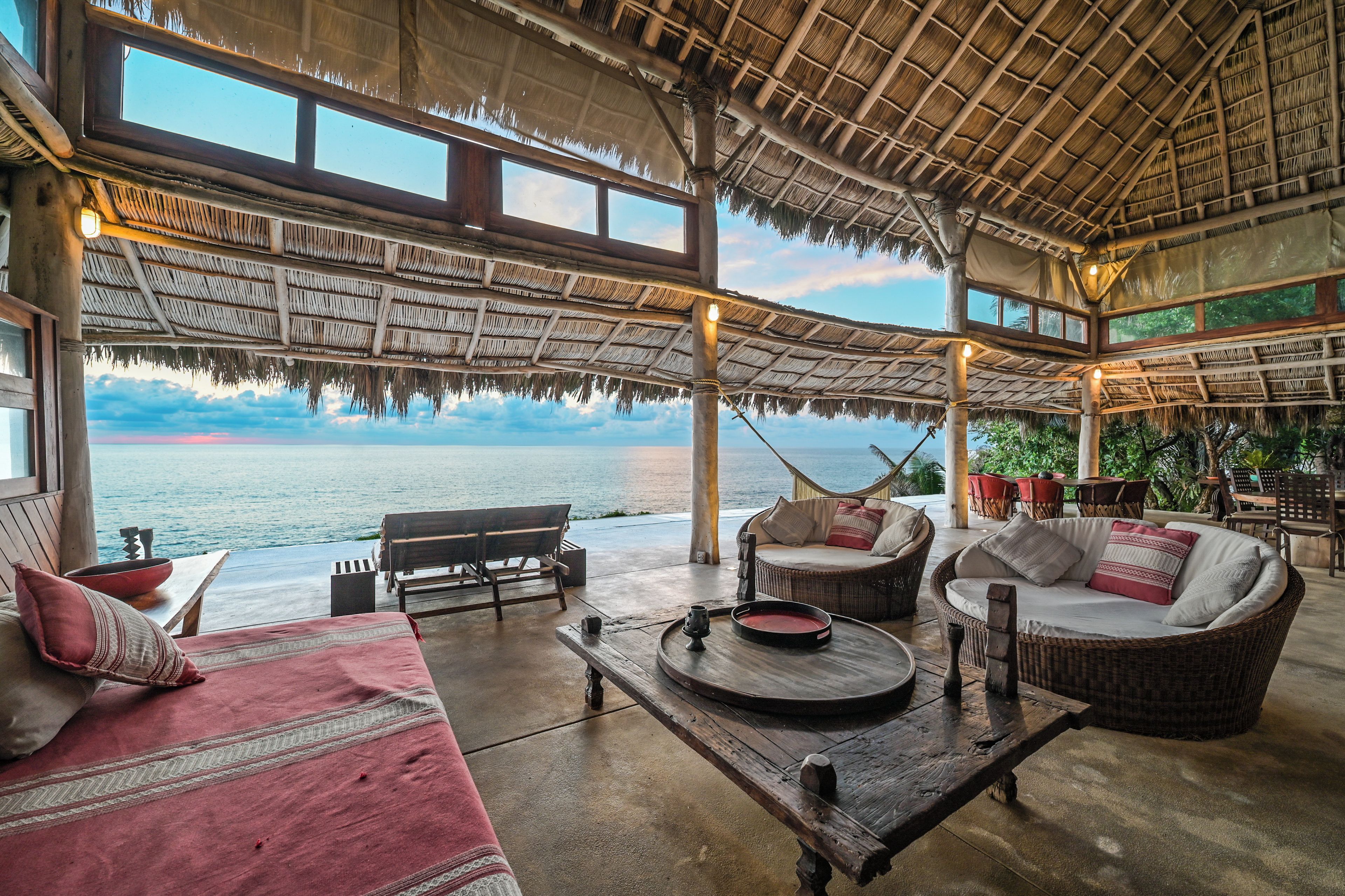 A beachside lounge with a thatched roof, wicker furniture, and a view of the sea.