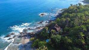 A coastal property with a swimming pool surrounded by lush greenery and a rocky shoreline.