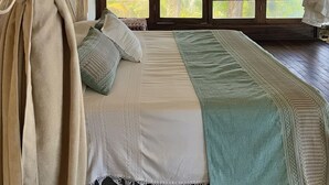 A bedroom with a bed, curtains, and a view of palm trees.