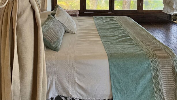 Quarto com cama, cortinas e vista para palmeiras.