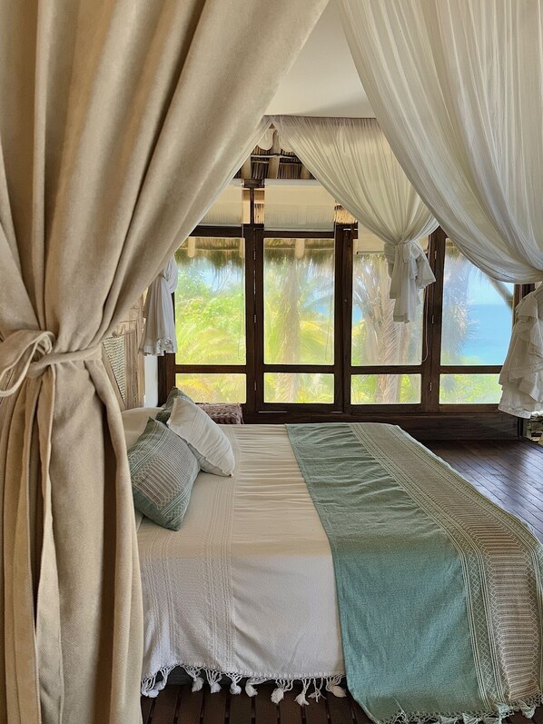 A bedroom with a bed, curtains, and a view of palm trees. - Gran Palapa Ocean Front Beach with Privacy Nature (SAYULITA)