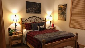 A bedroom with a wooden bed, two bedside tables with lamps, a bench, and artwork on the walls. - Summer Sale: Mountain Retreat in Grand Lake (Grand Lake)