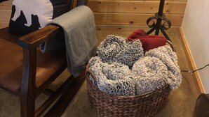 A wooden rocking chair with a cushion, a basket with blankets, and a floor lamp in a room with wooden paneling. - Summer Sale: Mountain Retreat in Grand Lake (Grand Lake)