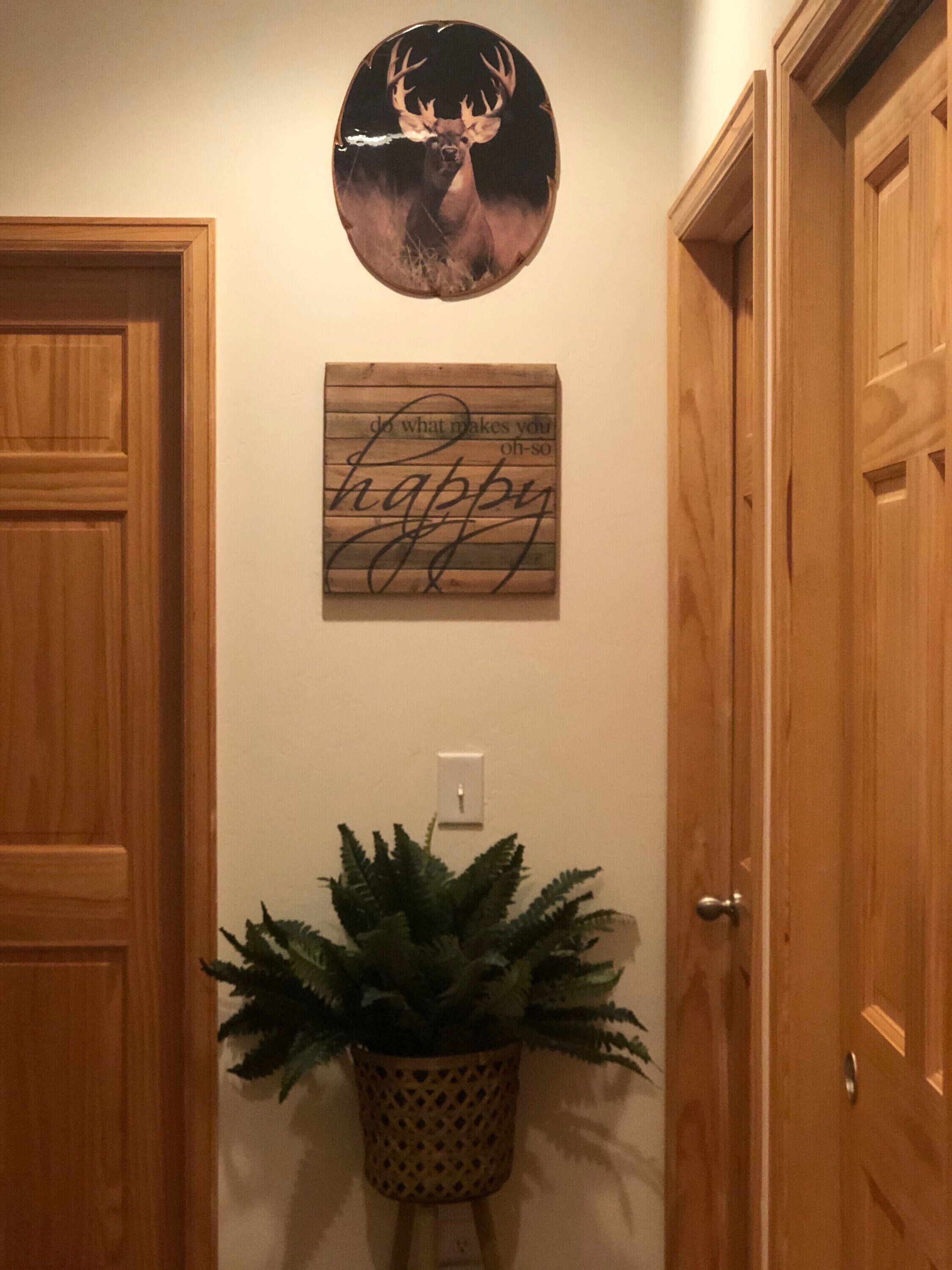 Ein Flur mit Holztüren, einem Wandbild von einem Hirsch, einem Spruchschild und einem Blumentopf.