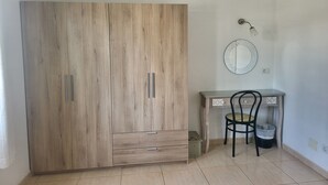 Een kamer met een houten garderobe, een bureau met stoel, een spiegel aan de muur en een hanglamp.