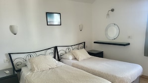 Een tweepersoonskamer met twee bedden, nachtkastjes, een spiegel aan de muur en een lijst met een foto.