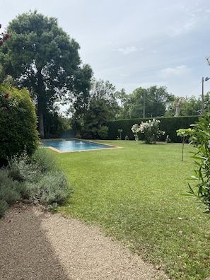 Un jardin à l’arrière de la maison, avec une piscine, entouré d’une pelouse bien entretenue et de diverses plantes.