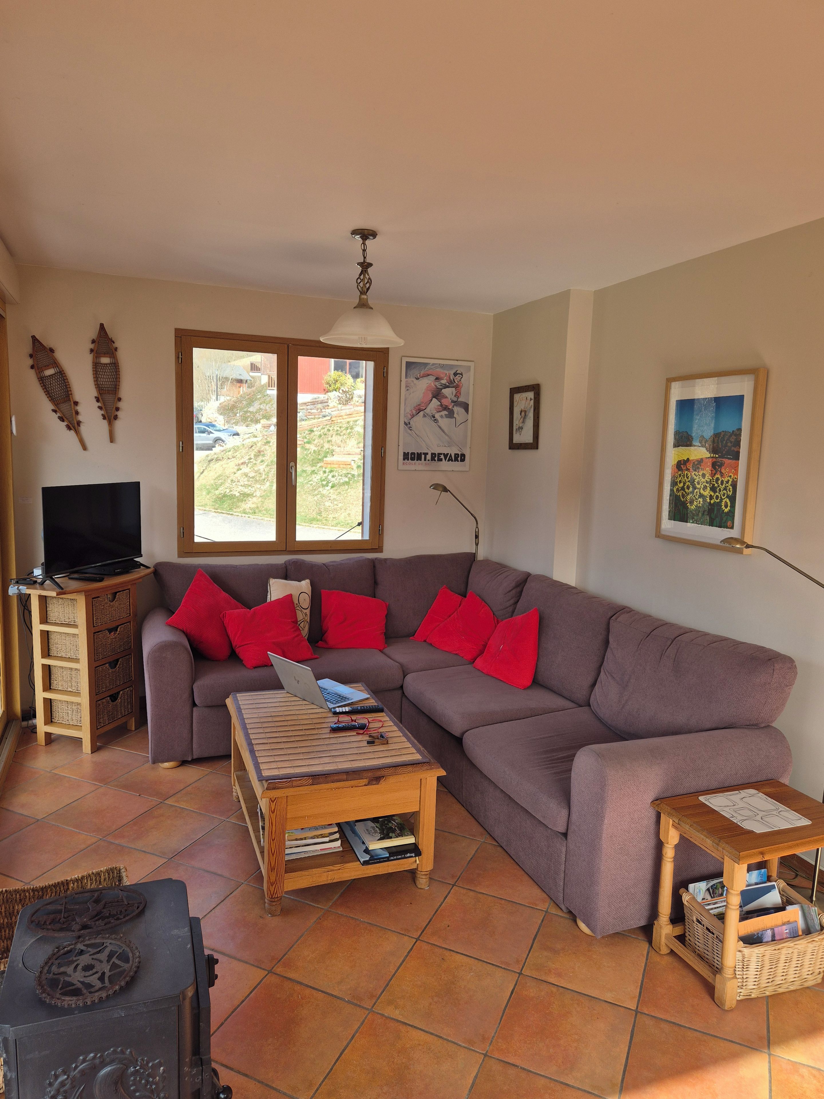 A living room with a sectional sofa, a wooden coffee table, a television on a stand, and a window with a view of the outdoors.