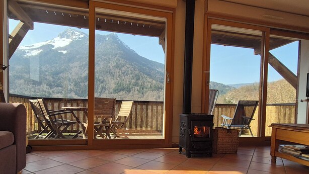 A room with a fireplace, a sofa, and a view of mountains through large sliding doors. - Cosy Chalet in the Real Alps near Annecy.
Relax, chill, walk, cycle, trek, ski. (Le Châtelard)