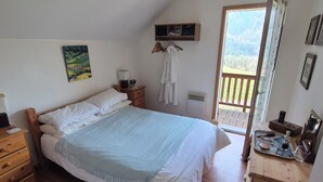 A bedroom with a bed, wooden dresser, bedside table, and a view of the outdoors. - Cosy Chalet in the Real Alps near Annecy.
Relax, chill, walk, cycle, trek, ski. (Le Châtelard)