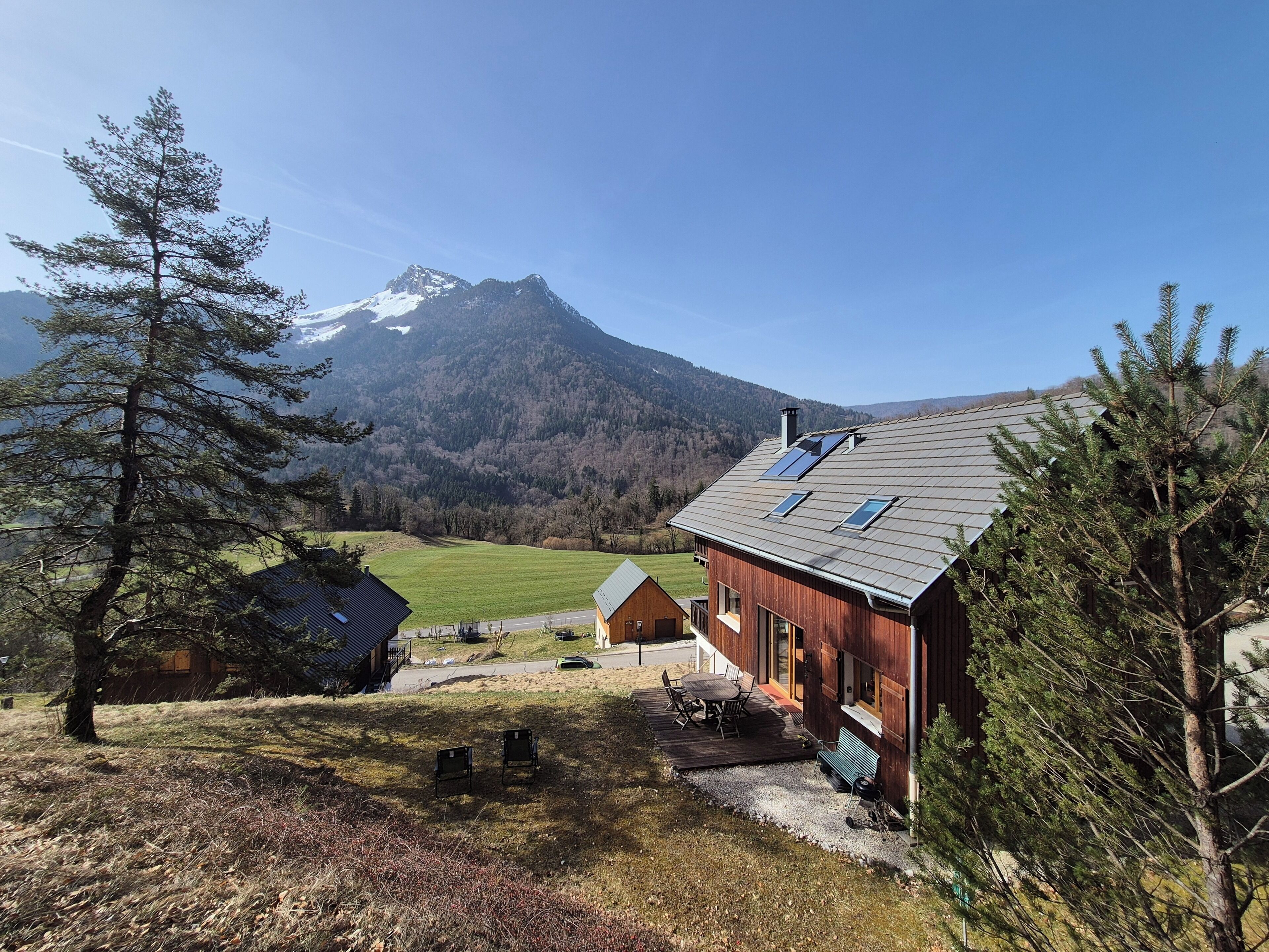 A wooden cabin with a deck, a mountain in the background, and a clear sky.