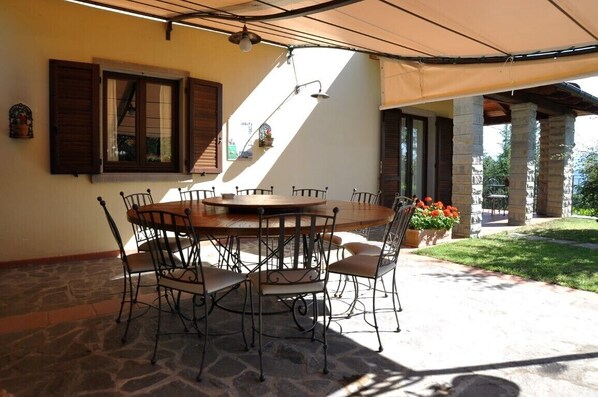 Un espacio de comedor al aire libre techado, con suelo de piedra, una mesa redonda de madera y sillas de metal.