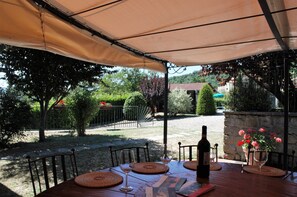 Een terras buiten met een eettafel, omringd door stoelen, en een fles wijn en een glas op de tafel.