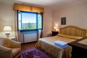 Een slaapkamer met een bed, een stoel, een raam met uitzicht, een radiator en een lamp.
