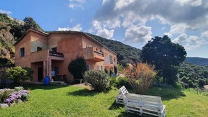 A two-story house with a balcony, surrounded by a well-maintained garden and a hilly landscape. - Apartment in a rustic atmosphere with sea views (Villanova)