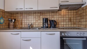 Eine Küche mit weißen Schränken, einer gefliesten Spritzschutzleiste, einer Kaffeemaschine und einem Backofen.
