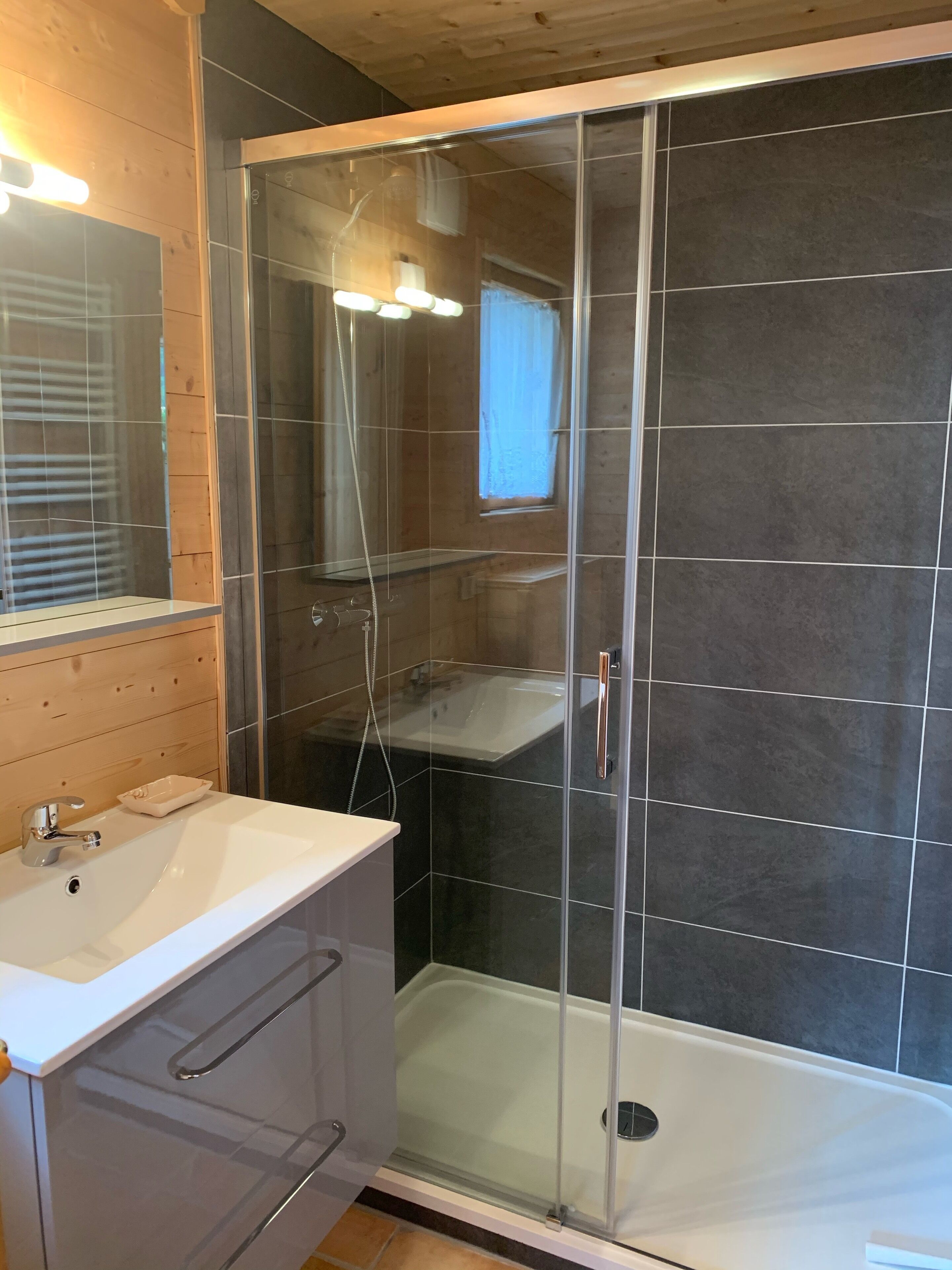 Een moderne badkamer met een douchecabine van glas, een witte wastafel en een houten opbergmeubel.
