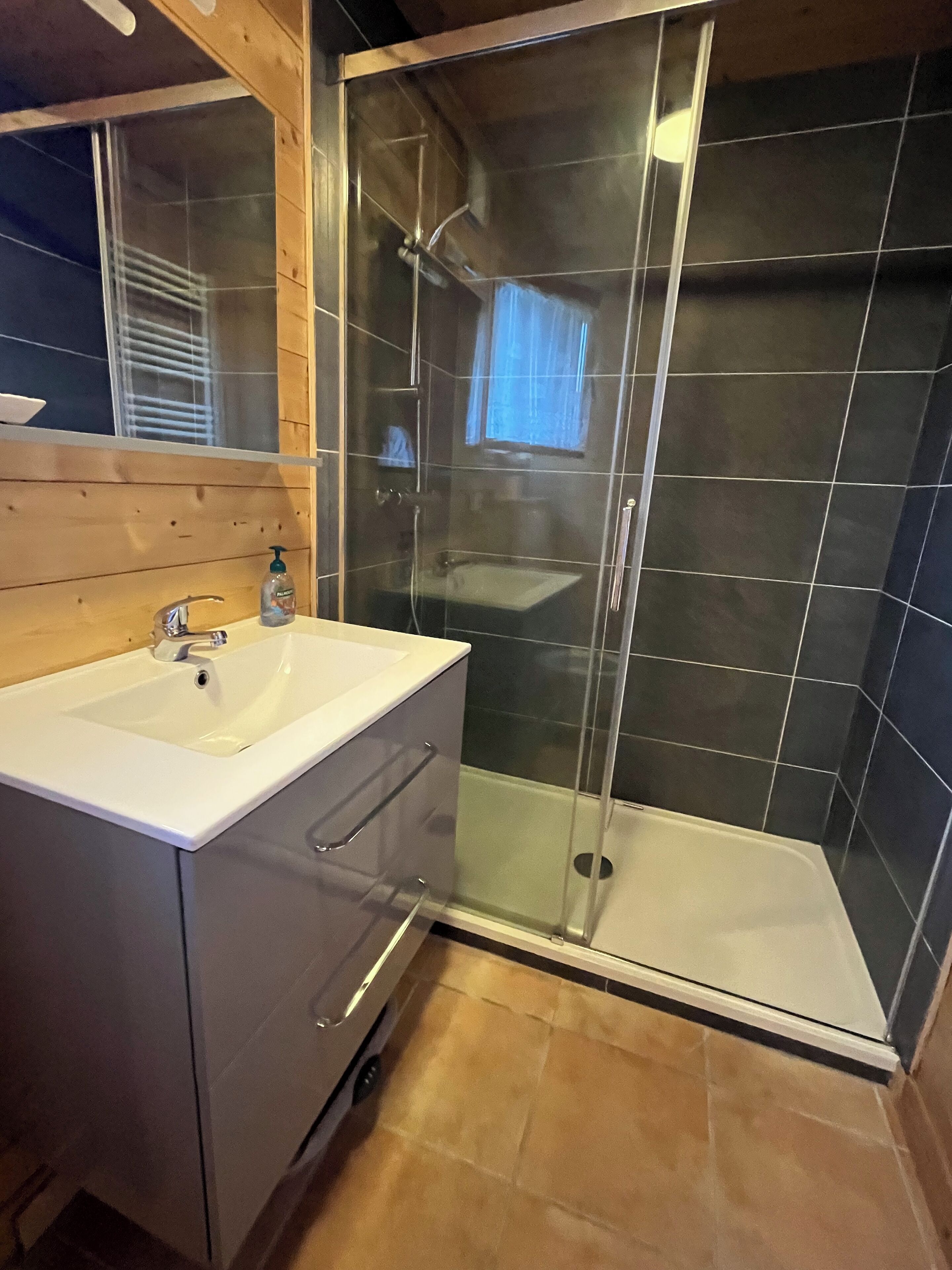 A modern bathroom with a glass-enclosed shower, a white sink, and a wooden vanity.