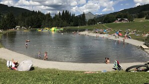 Un área junto al lago con piscina, zonas verdes y montañas al fondo.