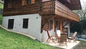 Una cabaña de madera con balcón, un patio con mobiliario exterior y un coche aparcado cerca.